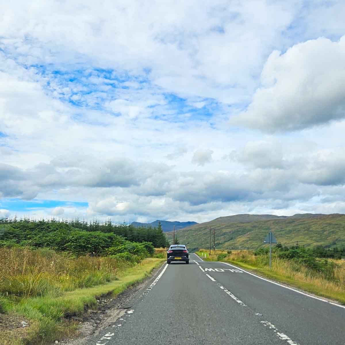 View of the open road driving through Scotland with a car on the road and hills in the distance - my tips for a Scotland road trip with kids and 12-day itinerary