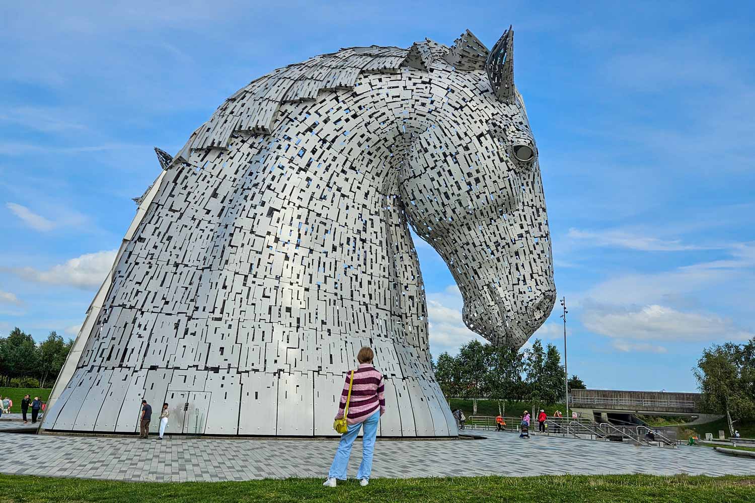 My daughter stands looking at the huge horse statues known as the Kelpies in Falkirk - one of the unmissable places to visit on a Scotland road trip with kids