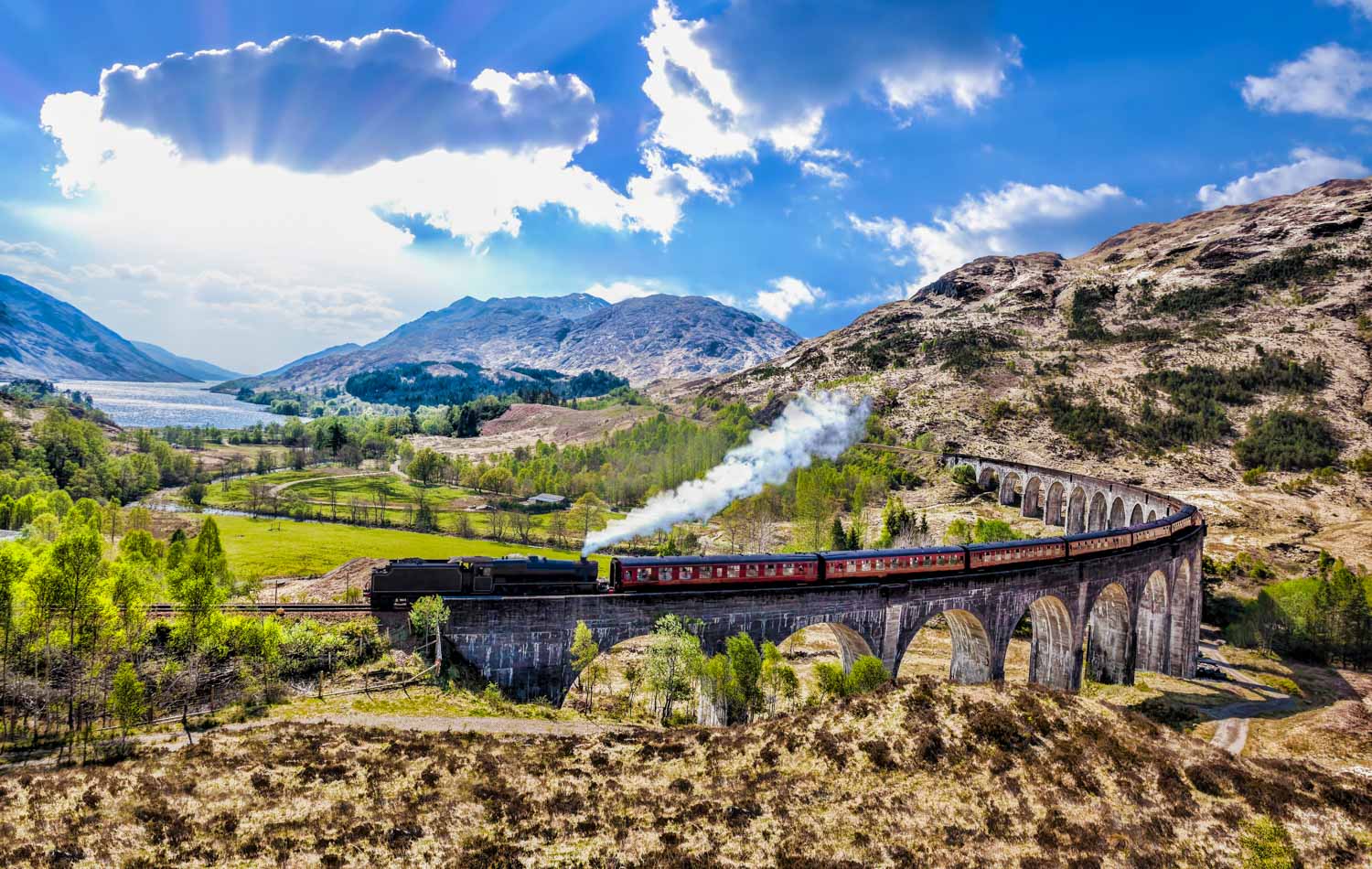 Glenfinnan Railway Viaduct in Scotland with the Jacobite steam train crossing the bridge - one of the great stops on a Scotland road trip with kids