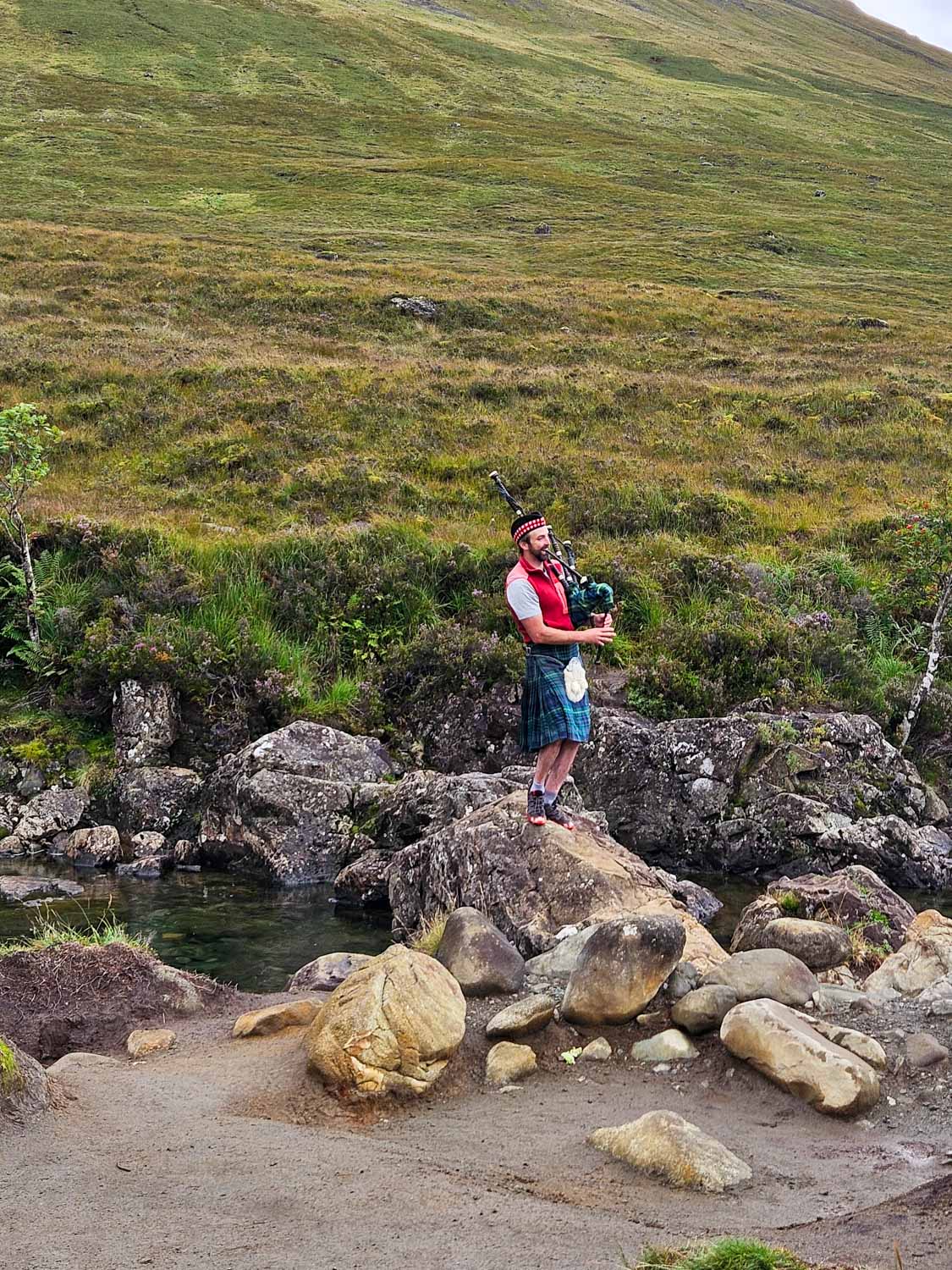 A piper plays the bagpipes while standing on a rock at the Fairy Pools - a visit is one of the best things to do in the Isle of Skye with kids