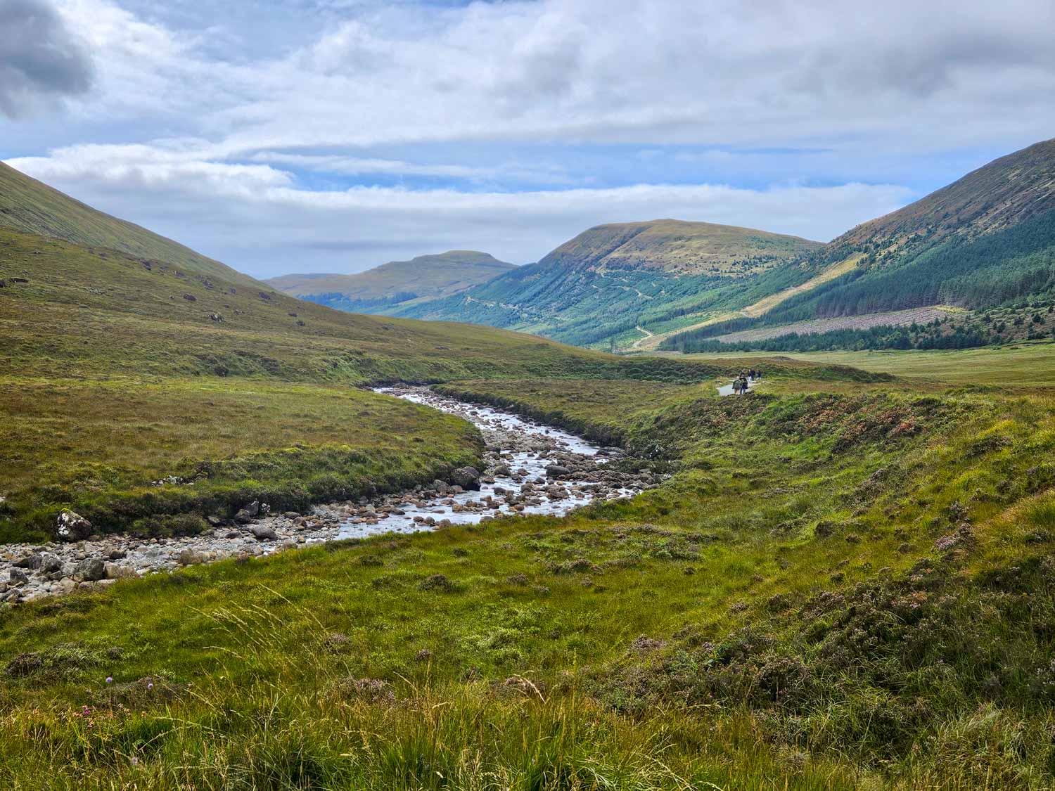 View through the valley including the shallow river and hills with some blue sky breaking through the clouds at the Fairy Pools - a visit is one of the best things to do in the Isle of Skye with kids