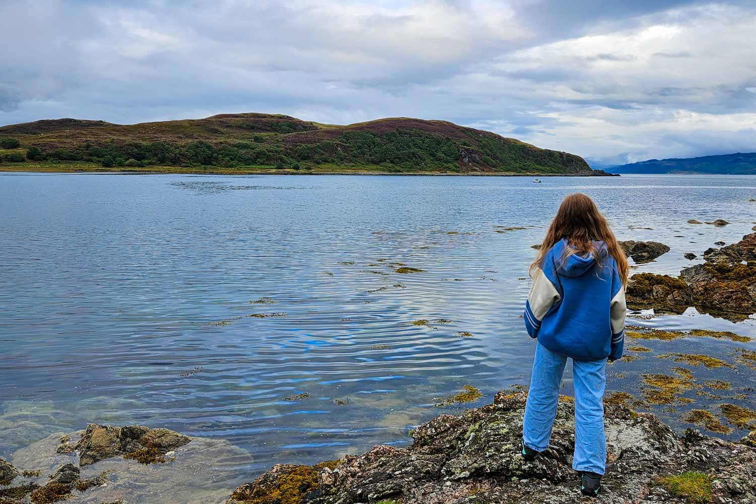 My daughter looks across the water near Isleornsay on the Isle of Skye to the hills beyond - my tips for the best things to do in the Isle of Skye with kids