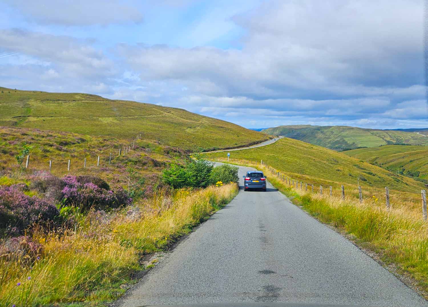 A car drives along a single track road through the hilly countryside in the Isle of Skye - my tips for visiting the Isle of Skye with kids