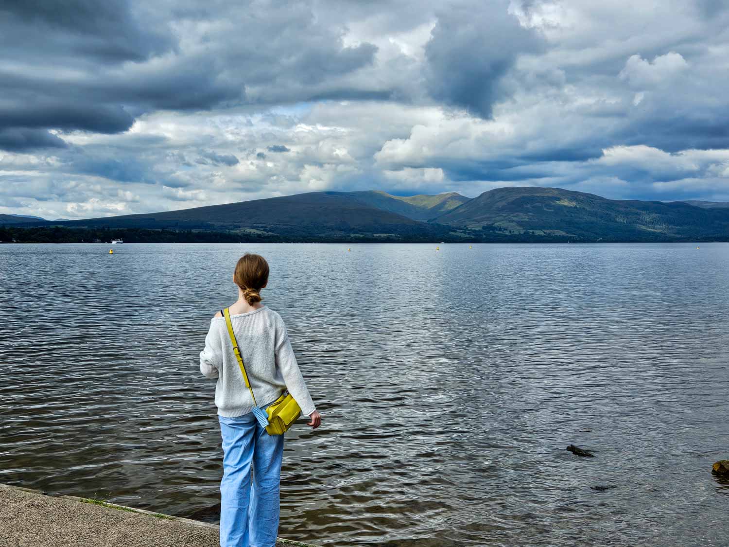 My daughter looks across Loch Lomond under a cloudy sky from Balloch Castle Country Park - a visit is one of the best things to do in Loch Lomond with kids