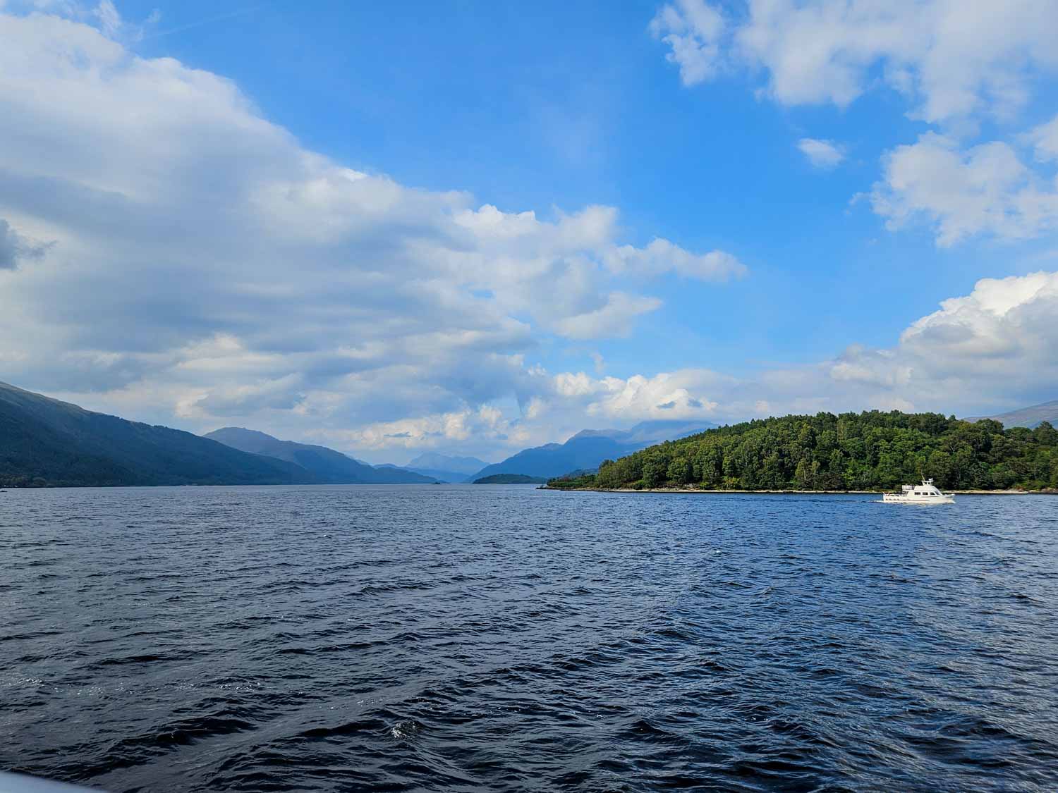 View across the blue waters of the loch to forested views and hills beyond - a boat trip is one of the best things to do in Loch Lomond with kids