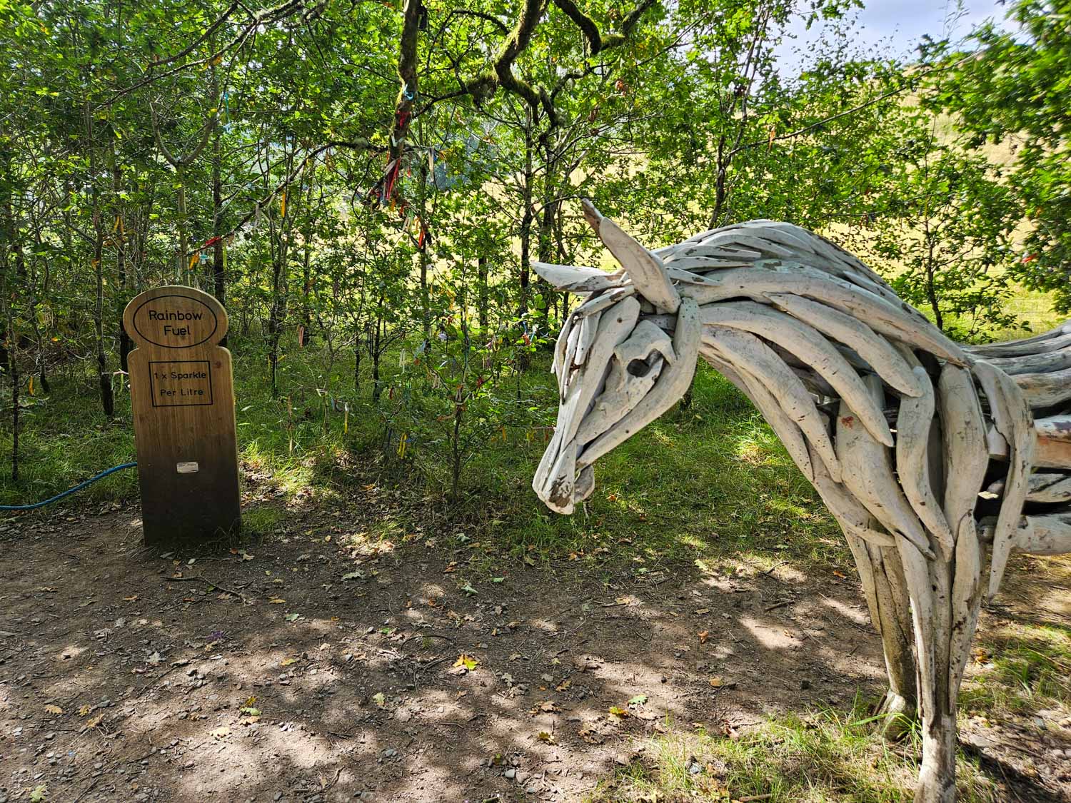Driftwood unicorn and sign reading rainbow fuel on a woodland trail near Luss - my pick of the best things to do in Loch Lomond with kids