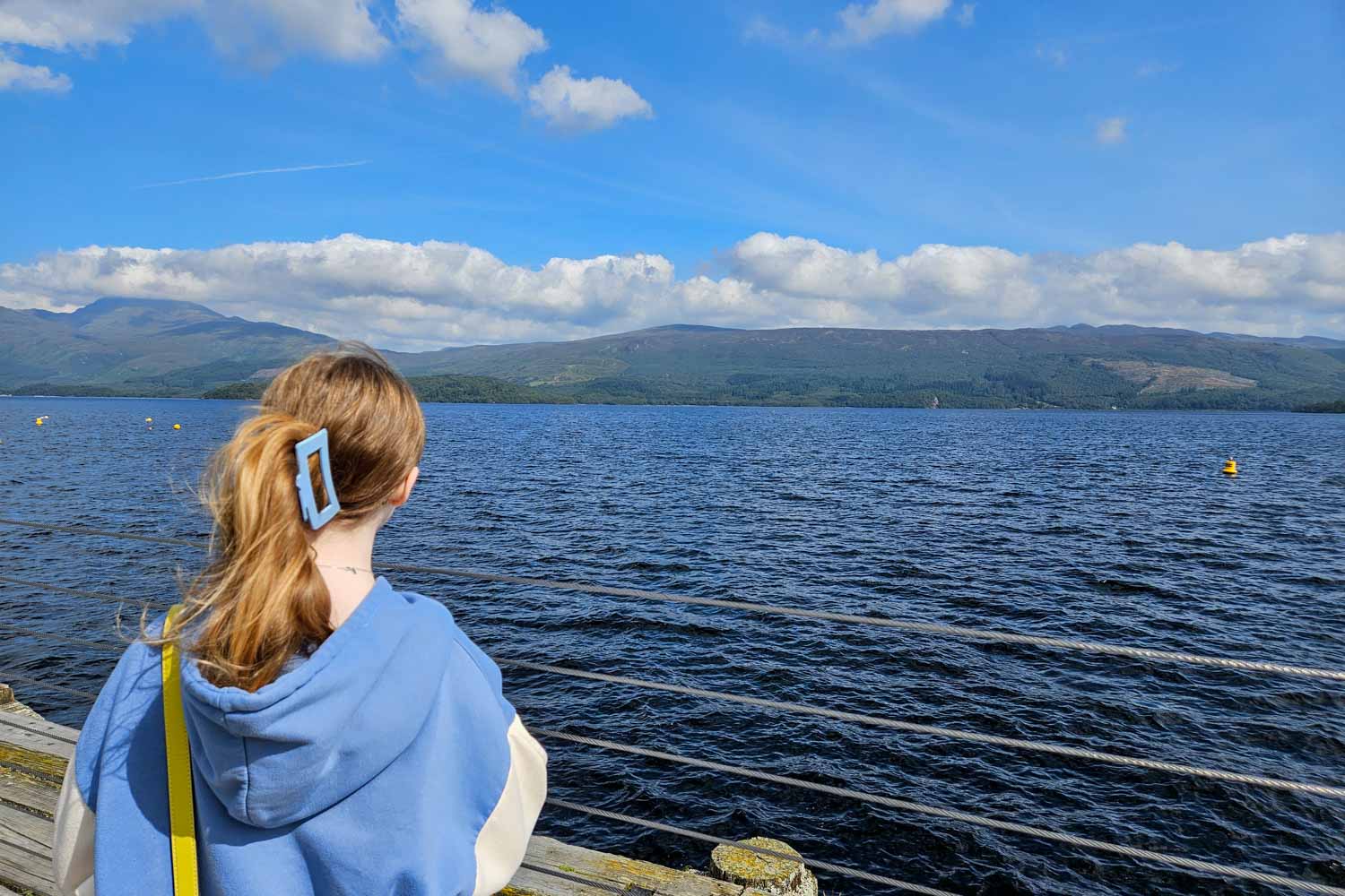 My daughter looks out onto the blue waters of Loch Lomond to the hills beyond - one of the beautiful places to visit on a Scotland road trip with kids