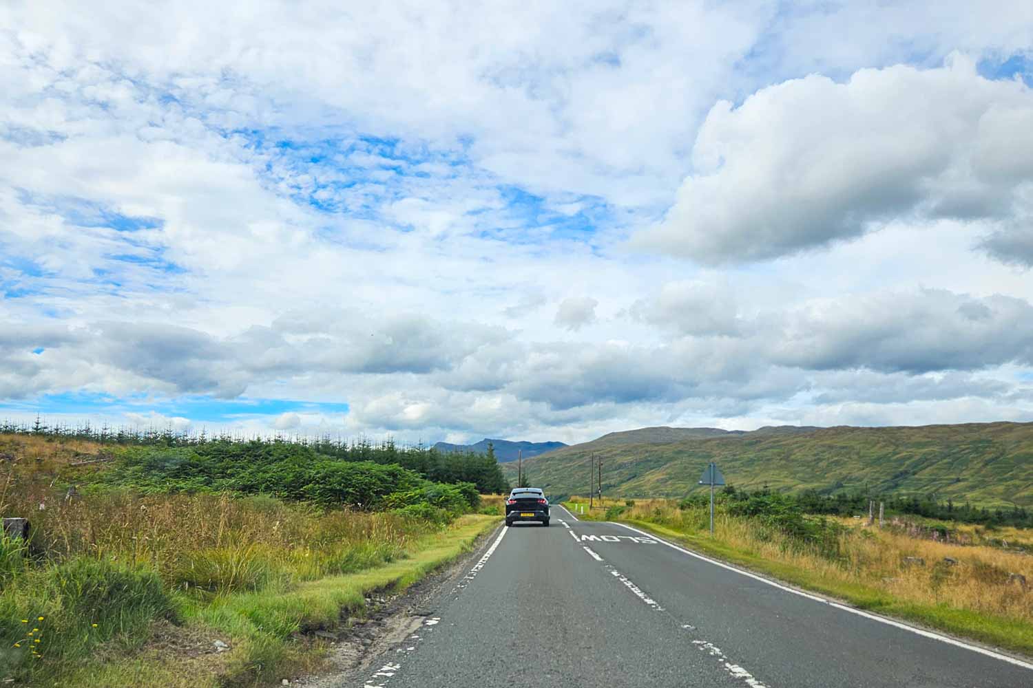 View of the open road driving through Scotland with a car on the road and hills in the distance - my tips for a Scotland road trip with kids and 12-day itinerary