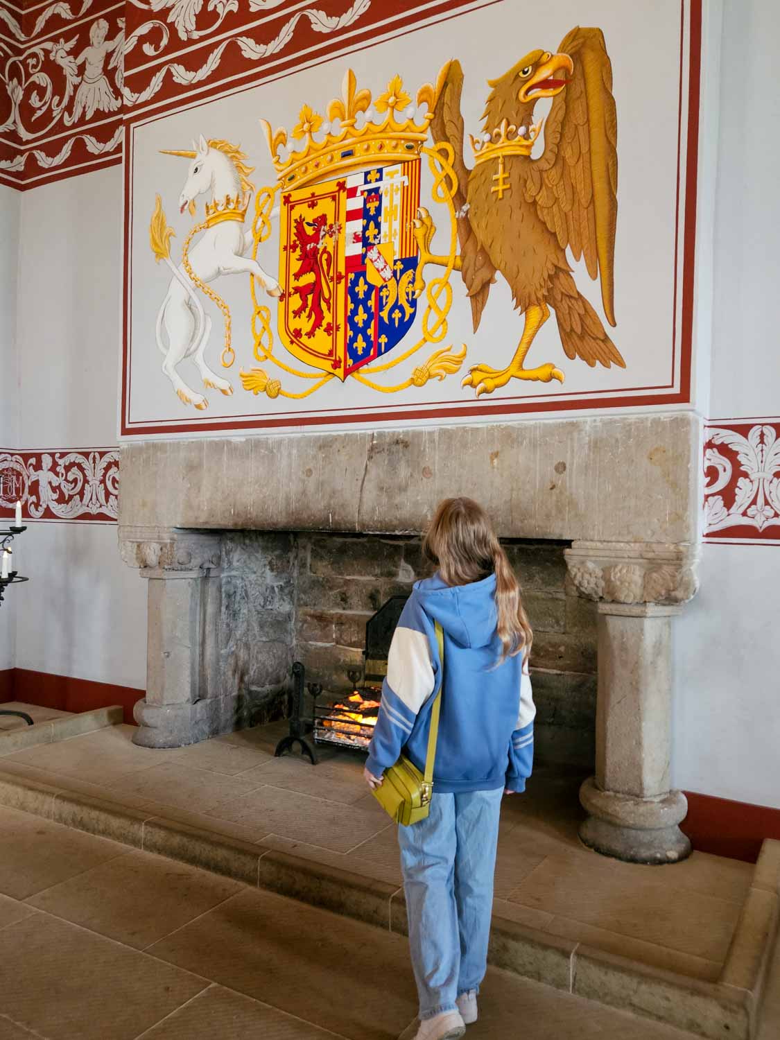 My daughter looks at the depiction of a unicorn and eagle above the huge stone fireplace in Stirling Castle - a visit is one of the best things to do in Stirling with kids