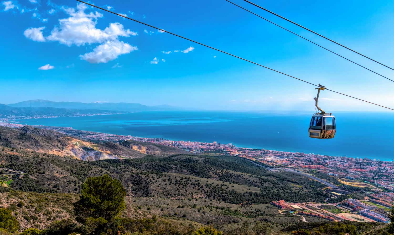 View of the Benalmadena cable car high above the hills with the city and sea in the background - a visit is one of the best day trips from Malaga with kids