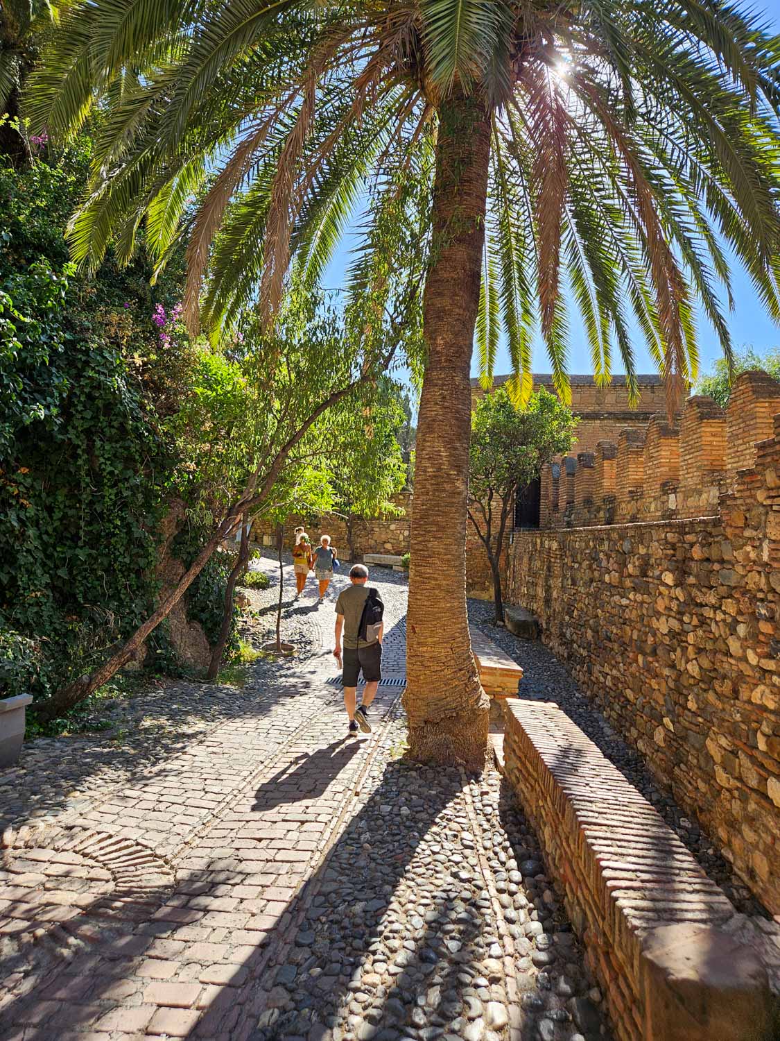 View of people walking along the cobbled path by the walls of the Alcazaba - a visit is one of the best things to do in Malaga with kids