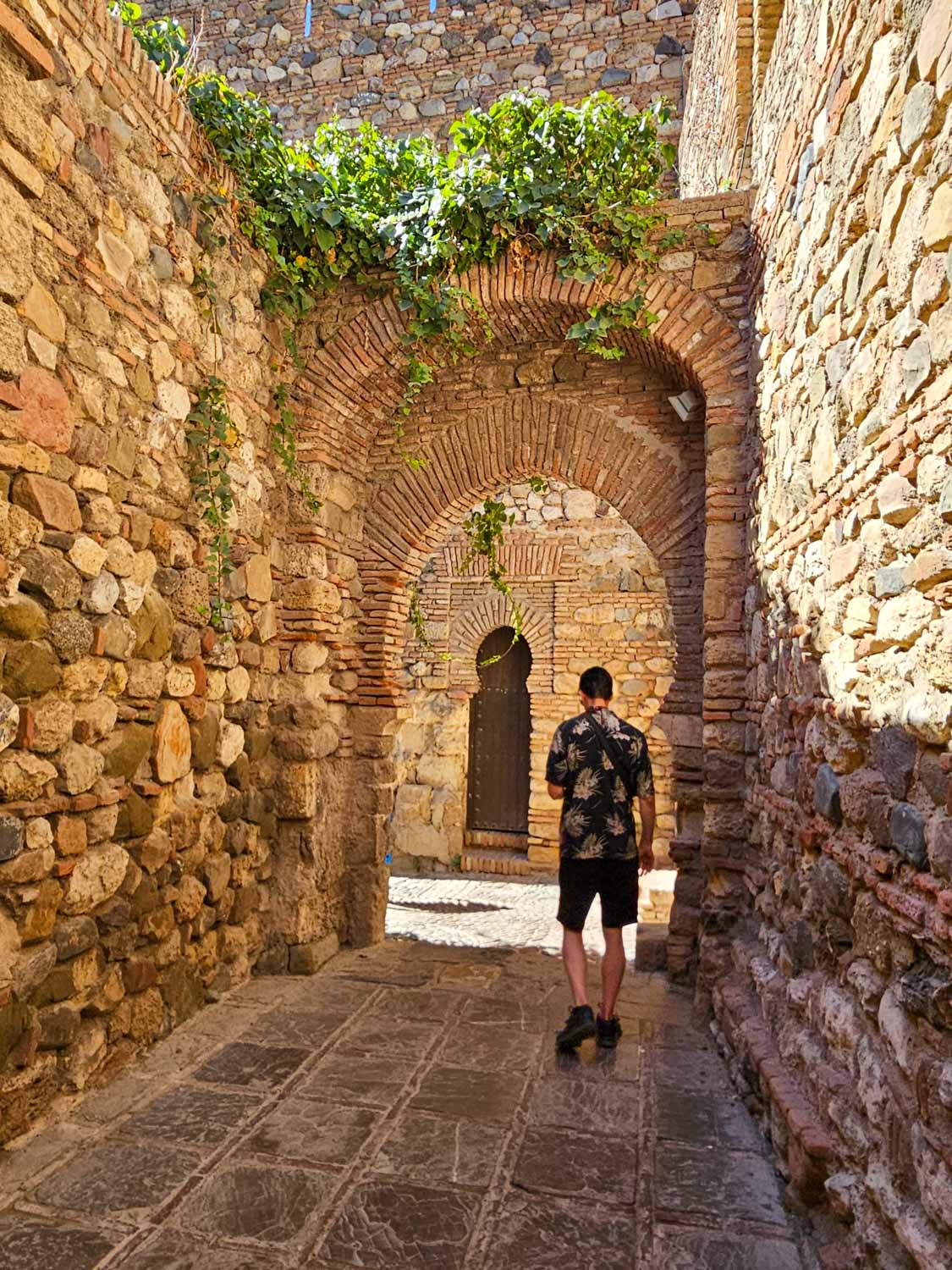 A man walks pst the old walls towards an archway in the Alcazaba palace-fortress in Malaga - one of the best places to visit in Malaga with kids