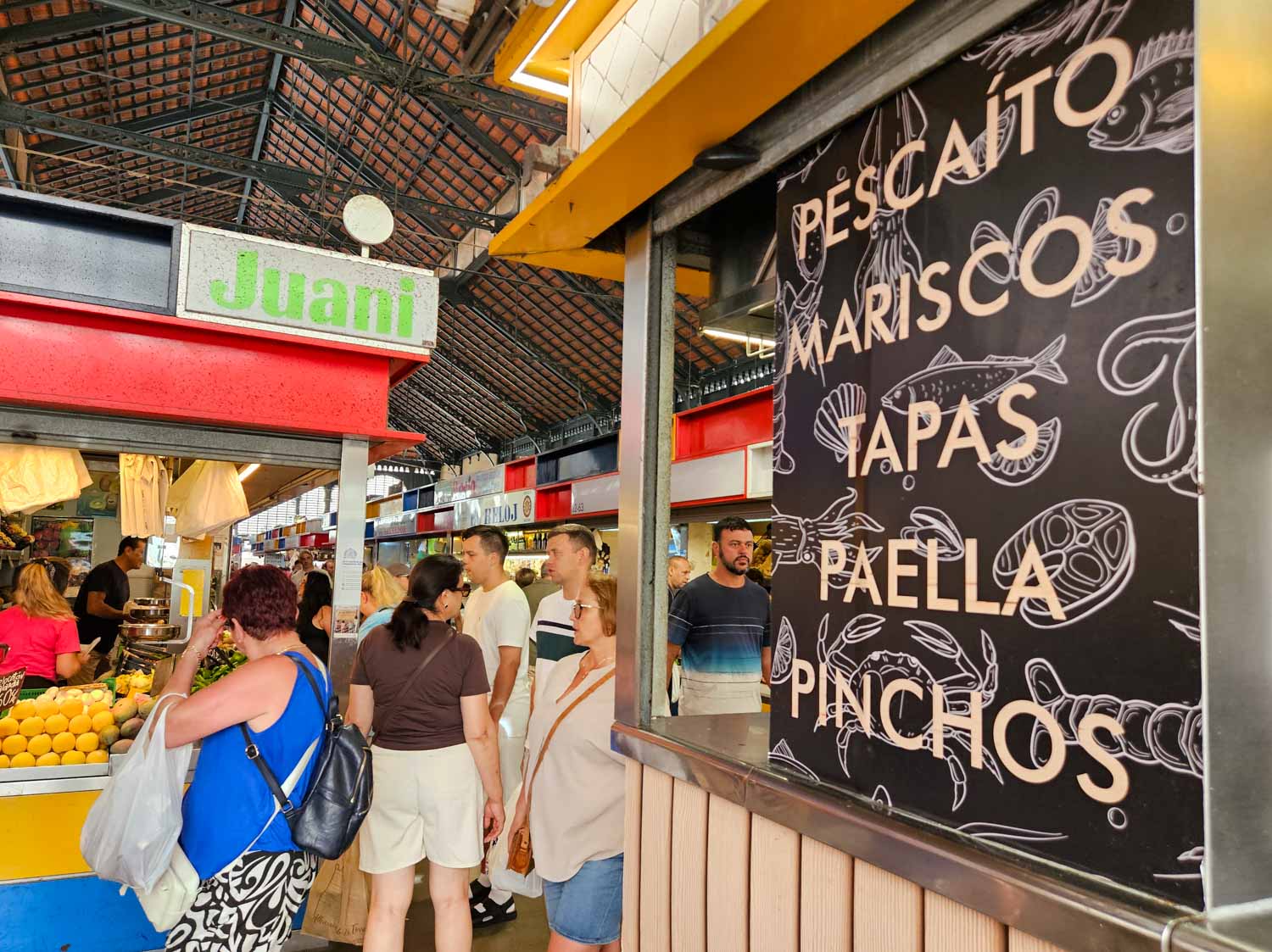 Sign reading pescaito, mariscos, tapas, paella, pinchos in Atarazanas market in Malaga with some of the stalls visible behind - one of the best places to visit in Malaga with kids