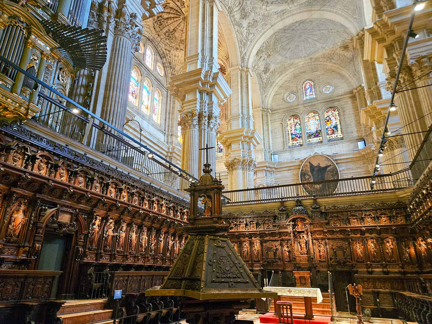 View of the carved wooden seats and stalls in the choir with the organ and stained glass windows also visible - one of the many places to visit in Malaga with kids