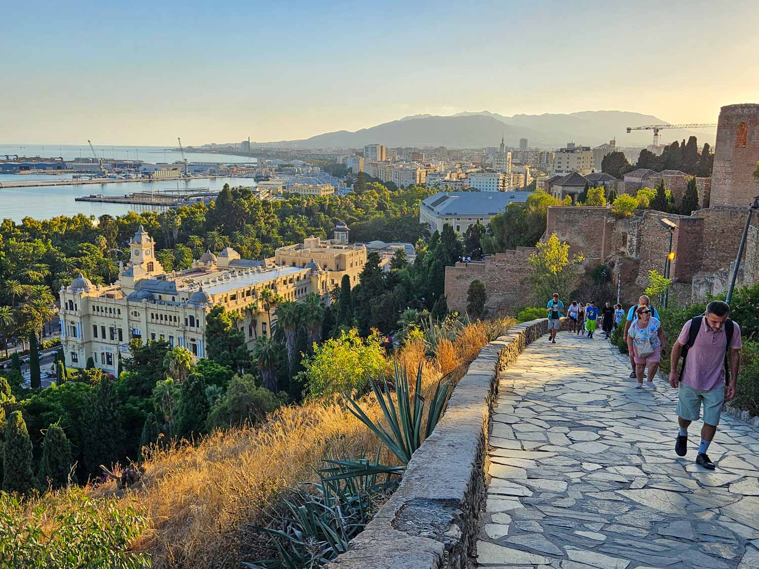 View of people climbing up the steep path to Gibralfaro Castle in time for sunset, with views of Malaga visible beyond - a visit is one of the best things to do in Malaga with kids