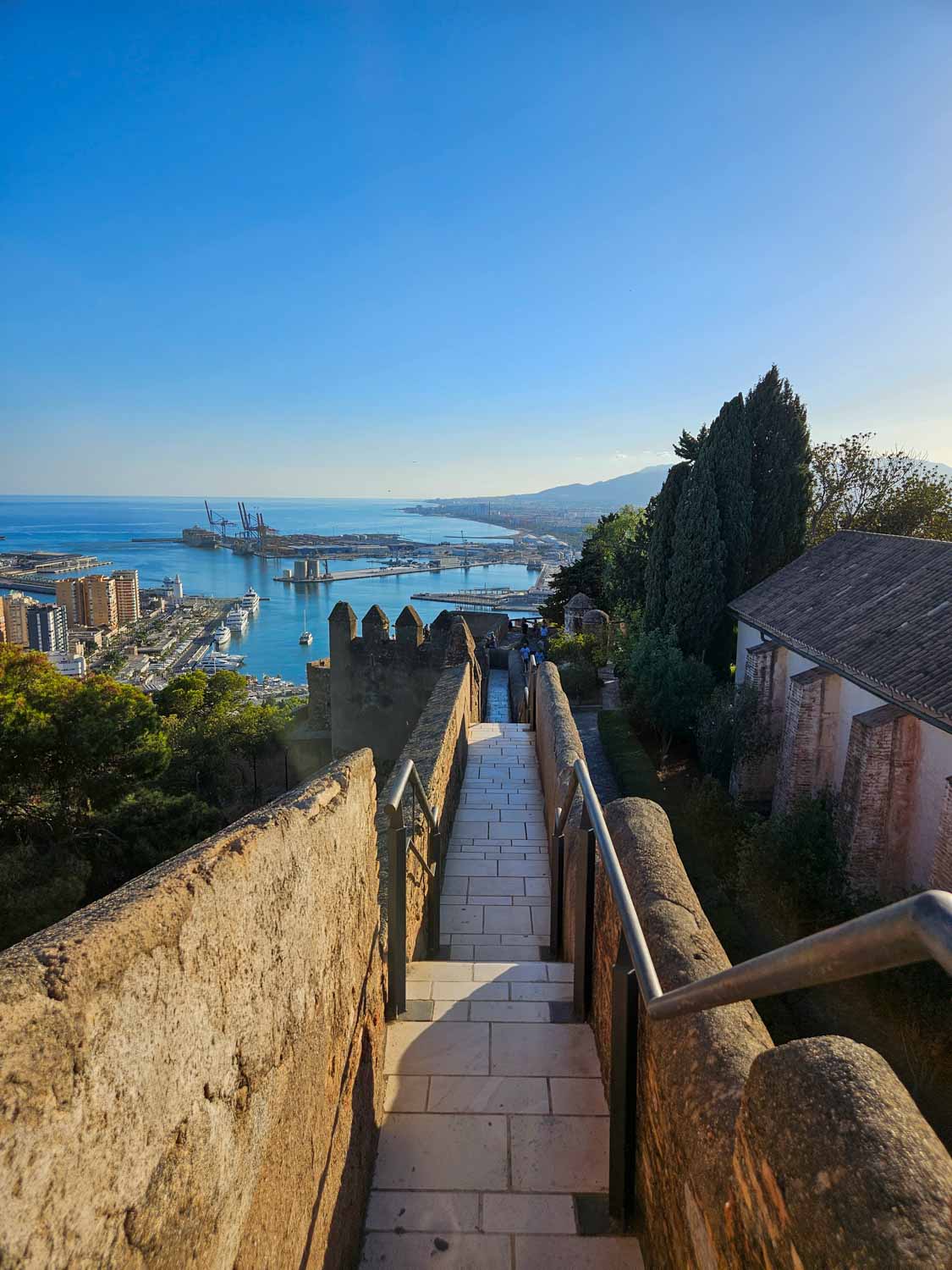 View down the narrow path leading to one of the towers of Gibralfaro Castle with the port and sea visible beyond - a visit is one of the best things to do in Malaga with kids
