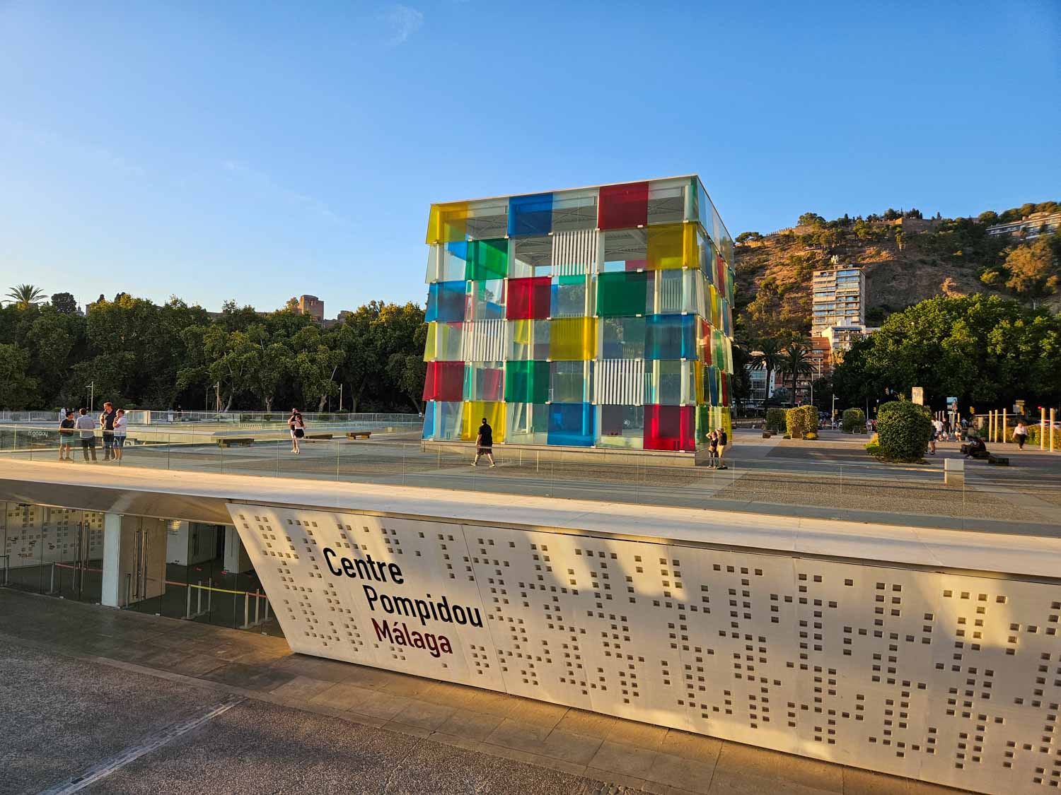 The multicoloured glass cube of the Centre Pompidou Malaga with the centre's entrance and sign visible on the level below - a visit is one of the many things to do in Malaga with kids