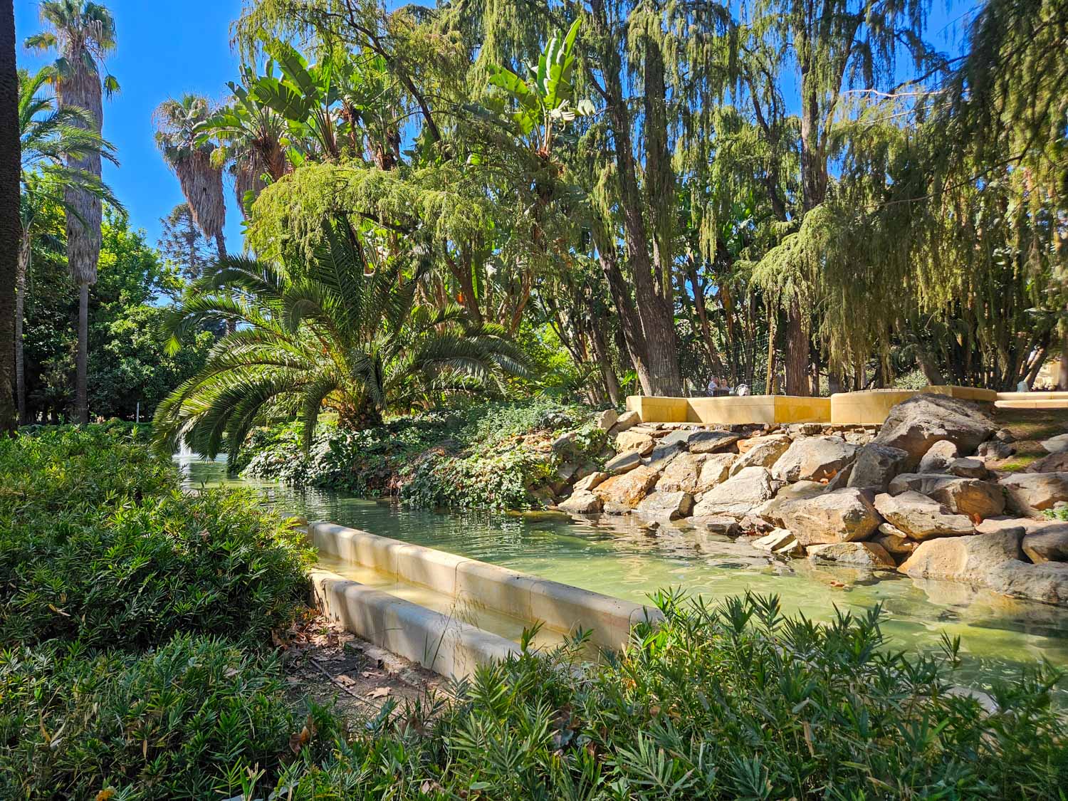 View of a water feature in Paseo del Parque, shaded by palm trees - a visit is one of the best things to do in Malaga with kids