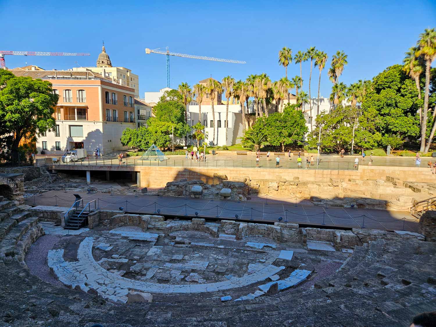 View from the stone seats down to the old stage of the Roman theatre and the glass pyramid of Malaga beyond - a visit is one of the best free things to do in Malaga with kids