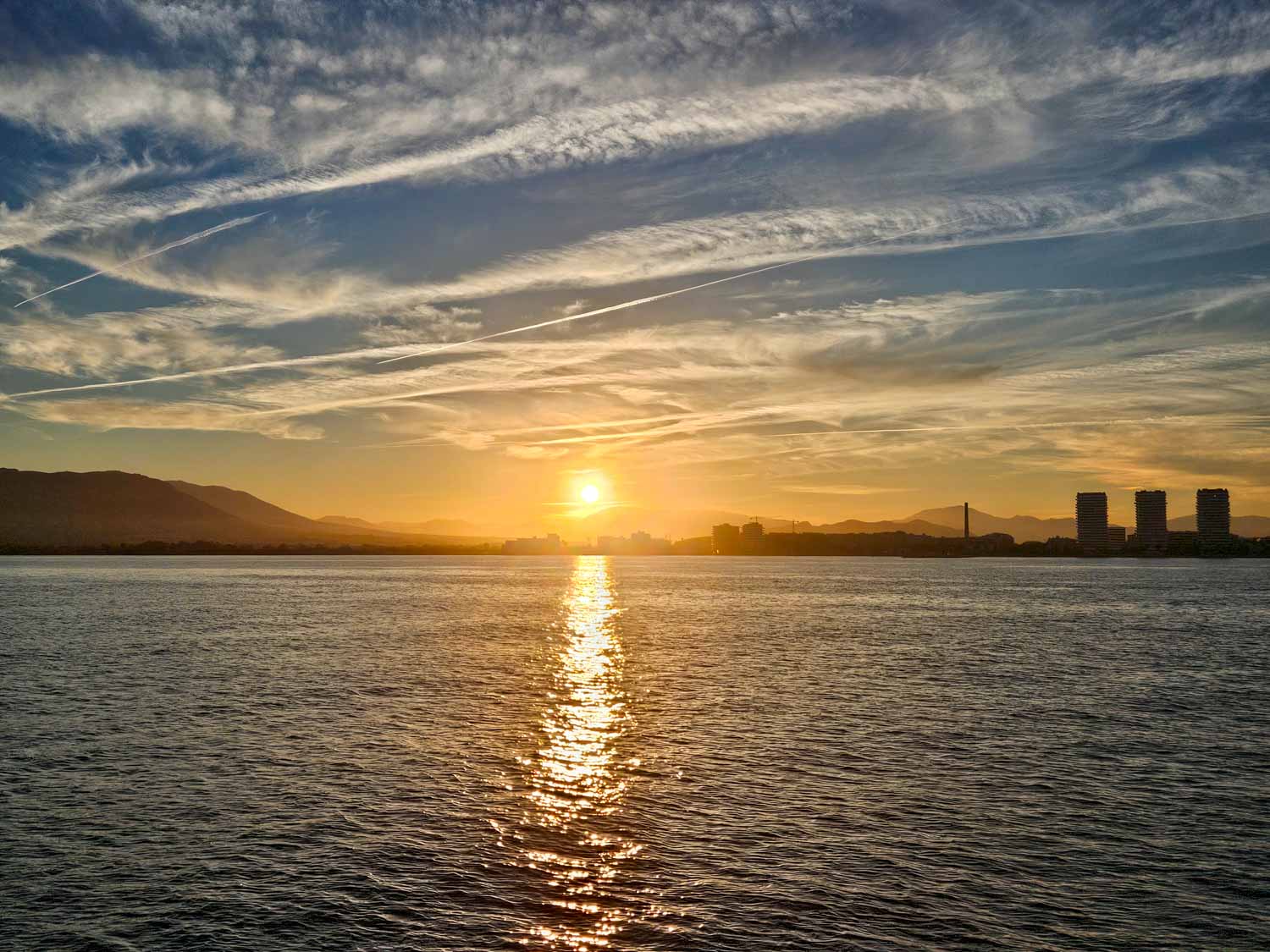Silhouetted buildings and hills with the setting sun reflecting in the sea on a sunset boat cruise - one of the best things to do in Malaga with kids