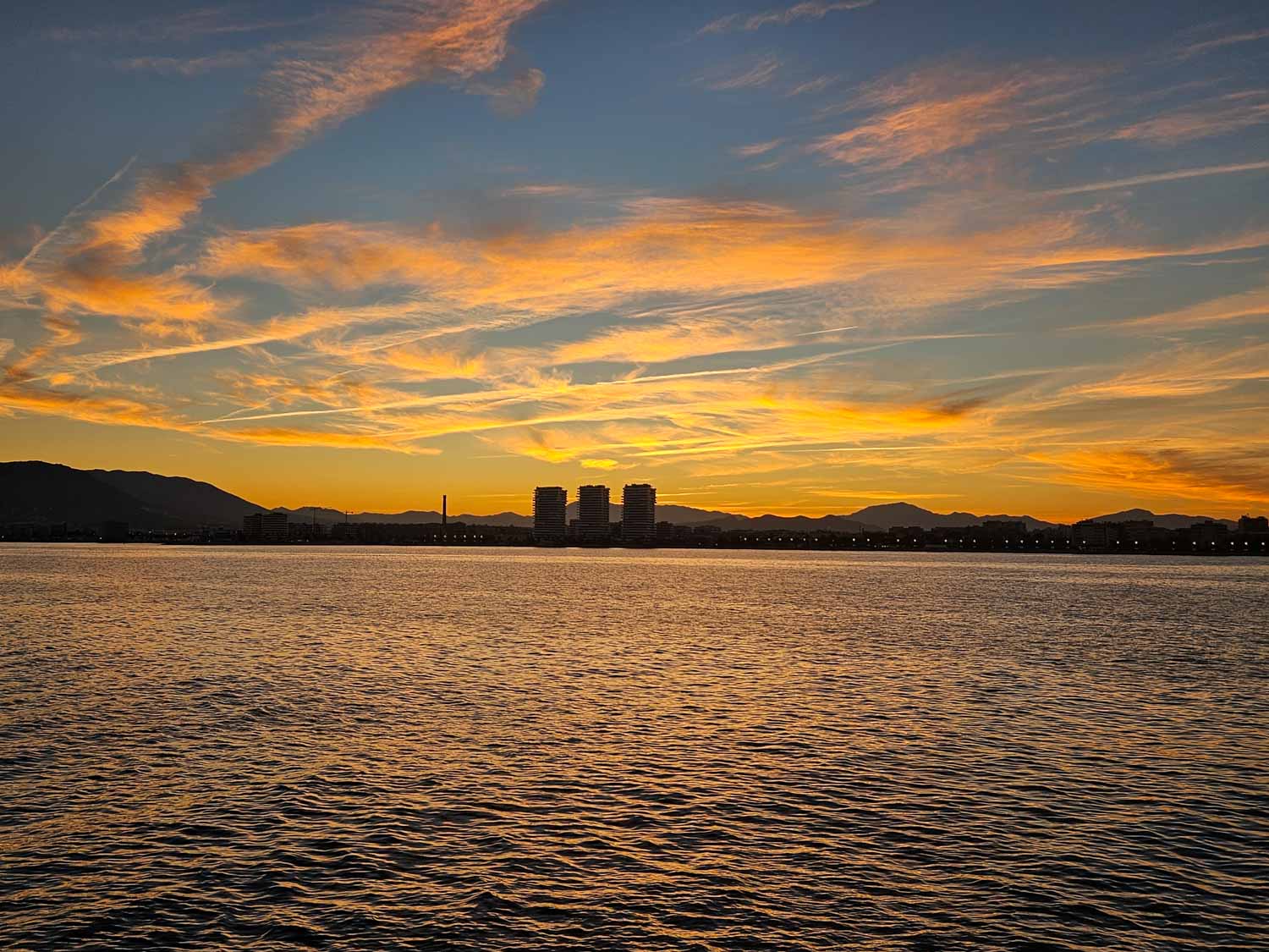 Gold and peach clouds over the silhouetted coastline seen from the water on a sunset boat cruise - one of the best things to do in Malaga with kids