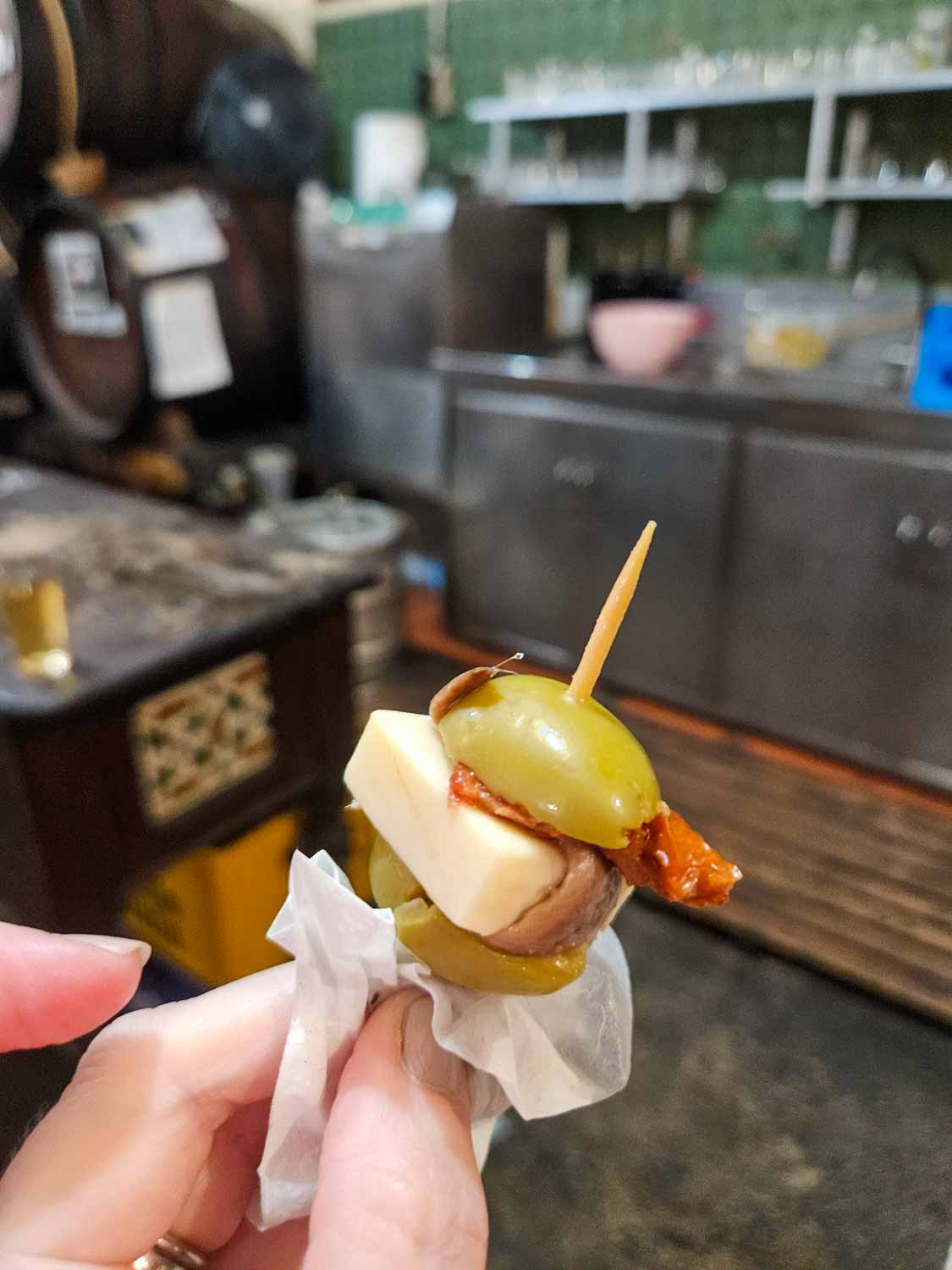 My hand holding a tapa of cheese, anchovy and olives on a stick during a tapas tour of Malaga