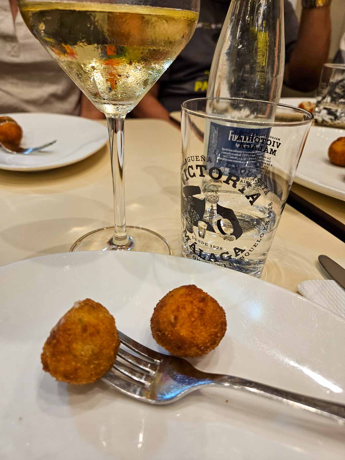 Two croquetas on a plate with fork and glass of white wine just seen - a tapas tour is one of the great things to do in Malaga with teens